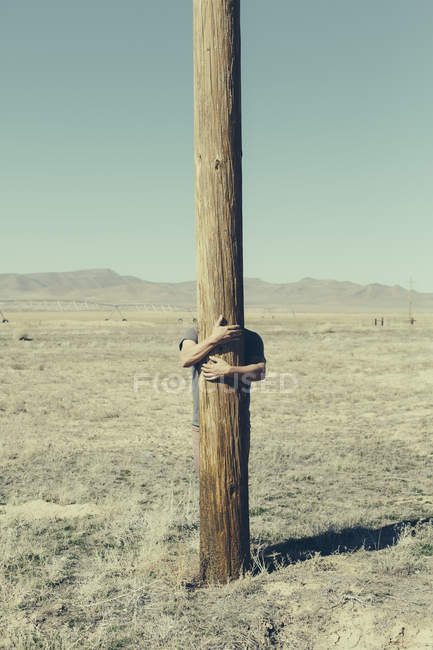 Man with his arms around wooden pole — Stock Photo