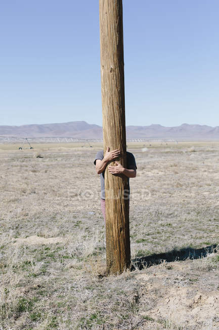 Hombre con sus brazos alrededor de poste de madera - foto de stock