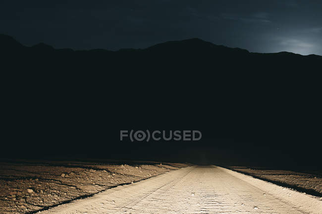 Estrada de terra no deserto iluminada por faróis de carro — Fotografia de Stock