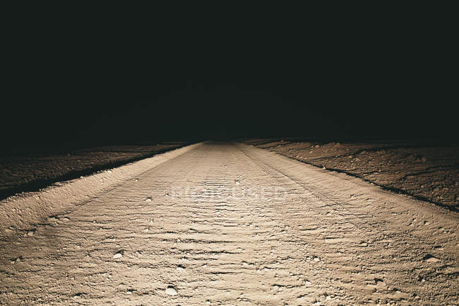 Dirt road in desert illuminated by car headlights — Stock Photo