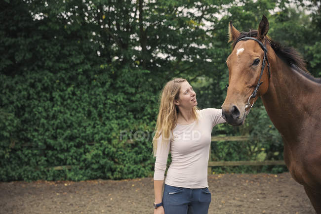 Frau tätschelt Pferd auf Koppel — Stockfoto