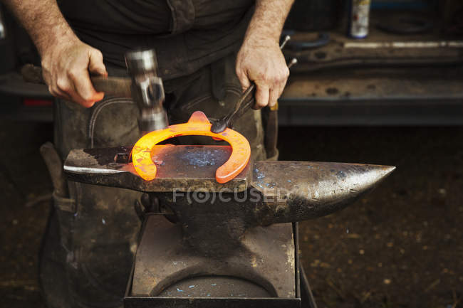 Herrero usando pinzas y martillo para sostener la herradura - foto de stock