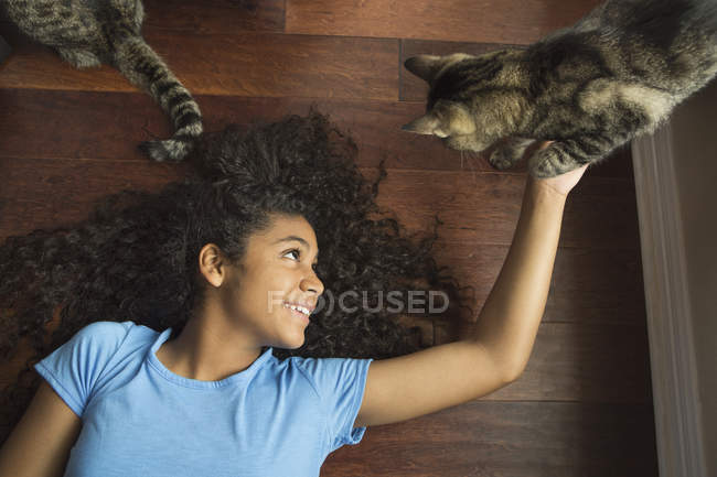 Girl lying on back stroking cat — Stock Photo