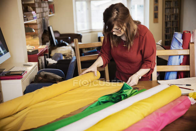 Женщина выбирает ткань из болтов на столешнице — стоковое фото