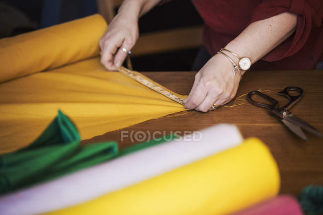 Woman using tape measure to yellow fabric — Stock Photo
