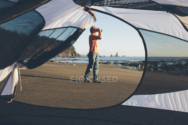 Uomo in piedi sulla spiaggia e guardando attraverso binocoli — Foto stock