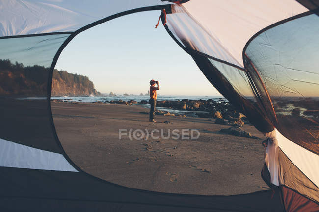 Man standing on beach and looking through binoculars — Stock Photo