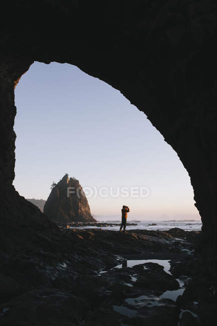 Homem de pé debaixo do mar caverna ao entardecer — Fotografia de Stock