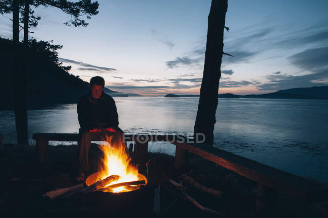 Mann sitzt in der Abenddämmerung am Lagerfeuer — Stockfoto