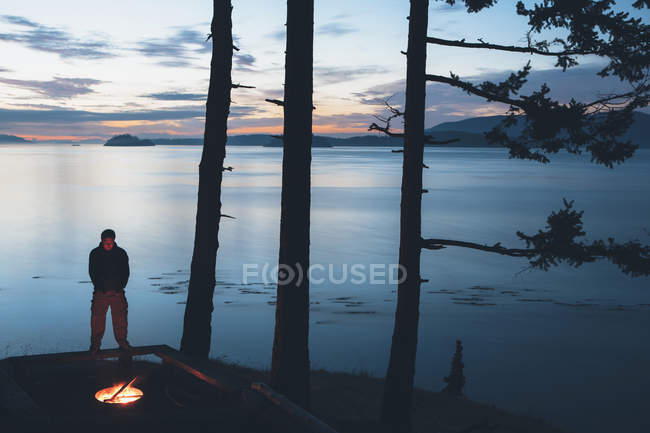 Homme debout près du feu de camp au crépuscule — Photo de stock