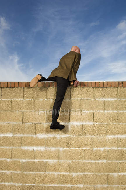 Homem escalando sobre parede de tijolo amarelo — Fotografia de Stock