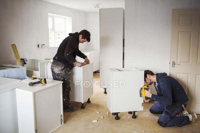 Bauarbeiter, die weiße Kücheneinheiten bauen. — Stockfoto