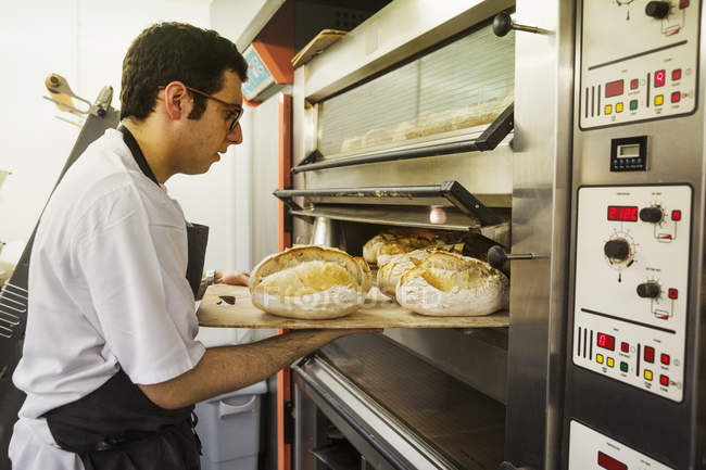 Пекарь снимает поднос с хлебом — стоковое фото