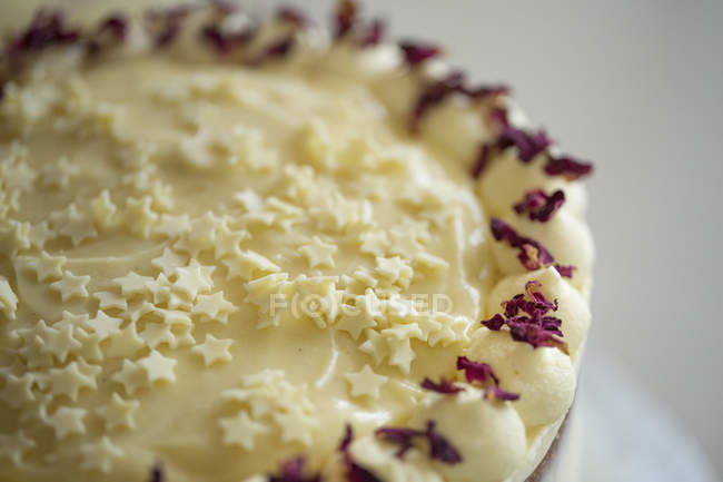 Торт со сливками и фиолетовыми лепестками цветов . — стоковое фото