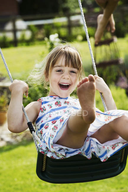Улыбающаяся девушка на качелях в саду . — стоковое фото