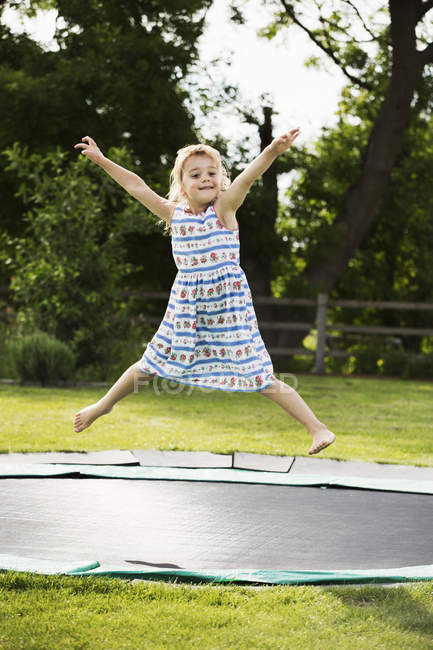Girl in sundress jumping on trampoline — Stock Photo