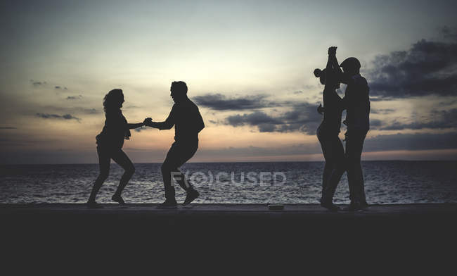 Quatro pessoas dançando à beira-mar em frente ao oceano ao anoitecer
. — Fotografia de Stock