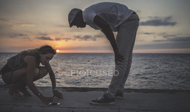 Two people looking at phone placed on seaside in front of ocean. — Stock Photo