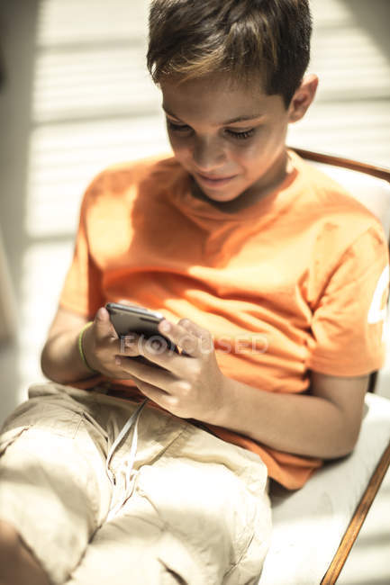 Мальчик, сидящий, глядя на мобильный телефон — стоковое фото