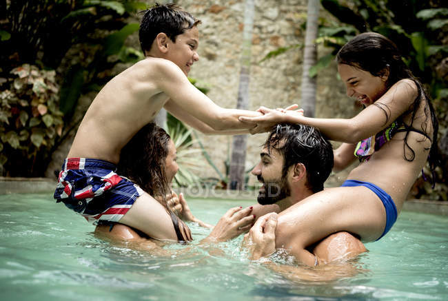 Children on shoulders of adults in swimming pool. — Stock Photo