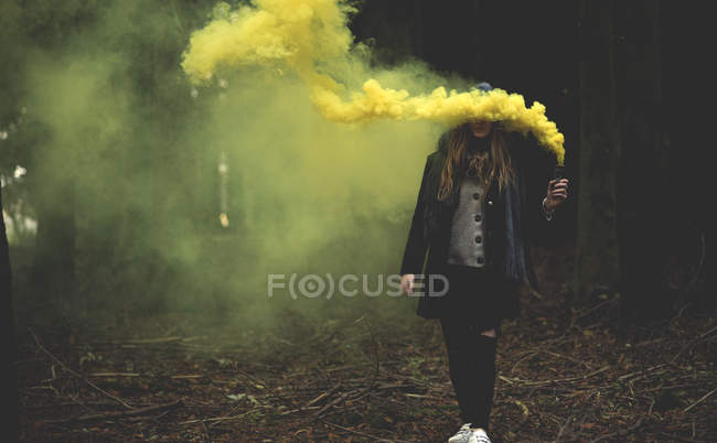 Femme tenant une fusée de fumée jaune dans la forêt . — Photo de stock