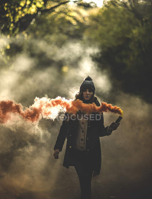 Woman holding orange smoke flare in forest. — Stock Photo