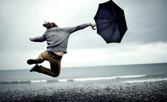 Man holding umbrella, jumping on beach — Stock Photo