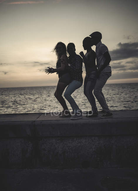 Четыре человека танцуют в очереди на фоне морской стены — стоковое фото