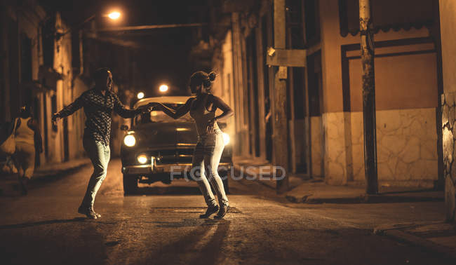 Mann und Frau tanzen nachts gemeinsam vor Oldtimer auf der Straße. — Stockfoto