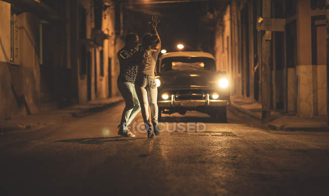 Homem e mulher dançando juntos na frente do carro clássico na rua à noite
. — Fotografia de Stock