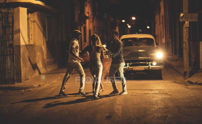 Gruppe von Menschen tanzt nachts vor einem Oldtimer auf der Straße. — Stockfoto
