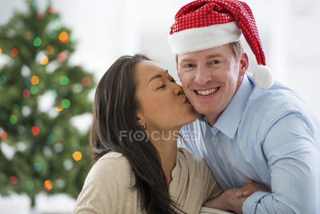 Coppia posa con Babbo Natale cappello davanti all'albero di Natale — Foto stock