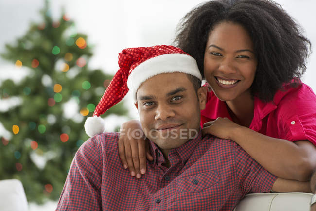 Africano casal americano posando com chapéu de Papai Noel na frente da árvore de Natal — Fotografia de Stock