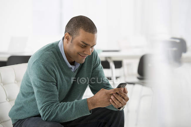 Чоловік перевіряє смартфон на дивані в офісі — стокове фото