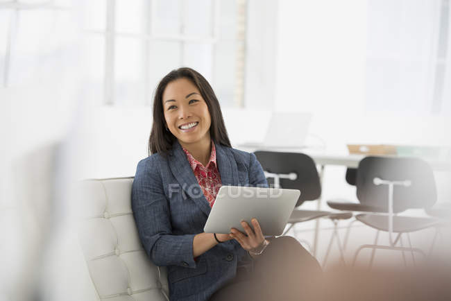 Mulher sentada no sofá com tablet digital e sorrindo na câmera — Fotografia de Stock