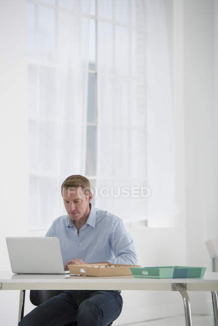 Человек сидит за столом и использует ноутбук в офисе — стоковое фото