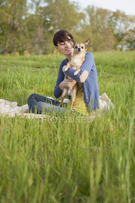 Vista lateral da mulher sentada na grama com cão chihuahua . — Fotografia de Stock