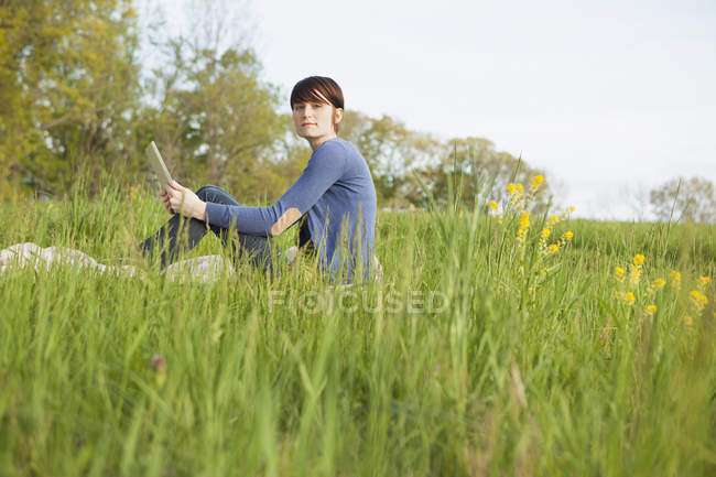 Seitenansicht einer Frau im Gras mit digitalem Tablet. — Stockfoto