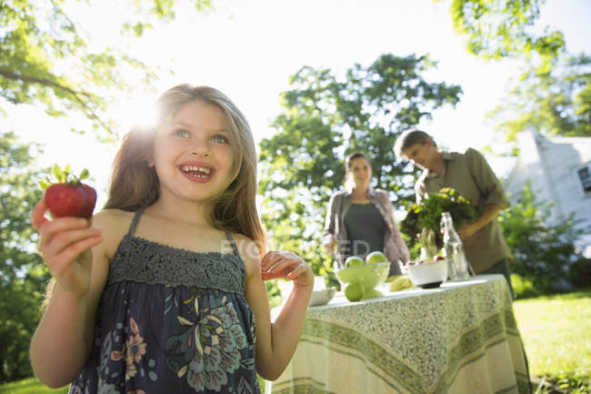 Девушка держит большой клубничный фрукт со взрослыми на заднем плане — стоковое фото