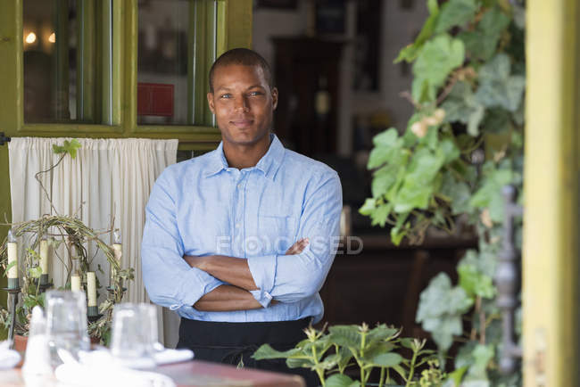 Man standing in front of open cafe with arms folded. — Stock Photo