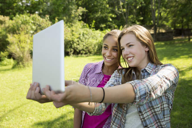Duas jovens mulheres tomando selfie com tablet digital no jardim — Fotografia de Stock