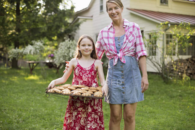 Mädchen hält Blech mit frisch gebackenen Plätzchen neben erwachsener Frau. — Stockfoto