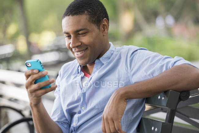 Homem sentado em um banco usando um smartphone . — Fotografia de Stock
