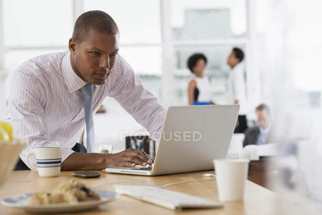 Uomo che utilizza laptop sulla scrivania in ufficio con colleghi irriconoscibili in background — Foto stock