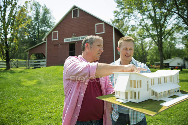 Maduro homem com adulto filho olhando para casa modelo no verde quintal — Fotografia de Stock