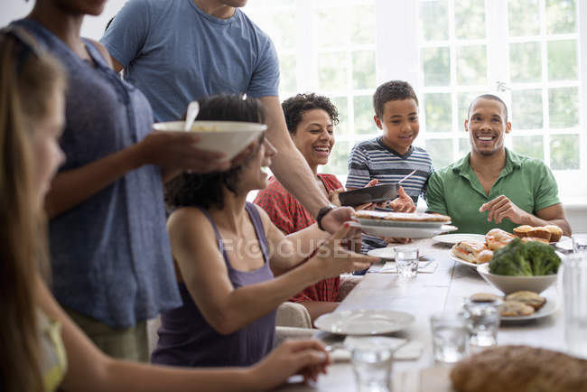 Сім'я чоловіків, жінок і хлопчиків обмінюються їжею за обіднім столом . — стокове фото