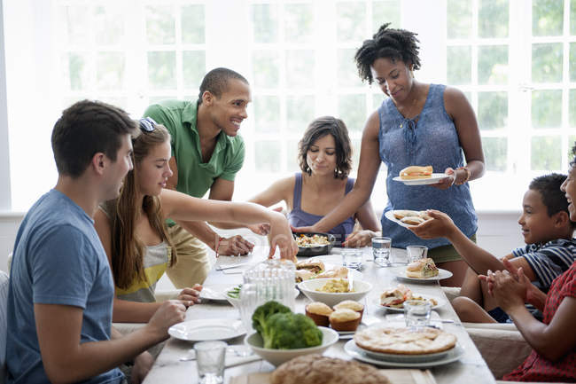 Familia de hombres, mujeres y niños compartiendo comida en la mesa de comedor . - foto de stock