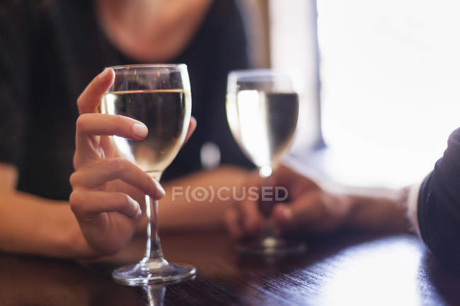Close-up of glasses of chilled white wine in hands of couple sitting in bar. — Stock Photo