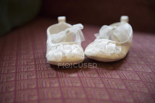 Pair of cream-colored embroidered satin Christening booties with lace ribbon bows. — Stock Photo