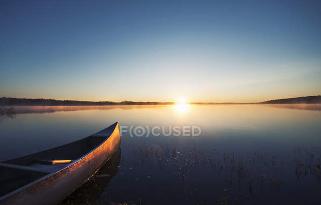 Canoa barco en superficie plana lago tranquilo al atardecer . - foto de stock